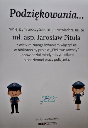 Na zdjęciu dyplom o treści: Podziękowanie Niniejszym uroczyście aktem zaświadcza się, że mł. asp. Jarosław Pituła z wielkim zaangażowaniem włączył się w biblioteczny projekt &quot;Ciekawe zawody&quot; i opowiedział młodym czytelnikom o codziennej pracy policjanta. Na dole Pieczątka dyrektora biblioteki oraz miejscowość i data: luty 2023. Po bokach dyplomy rysunek policjanta i policjantki.