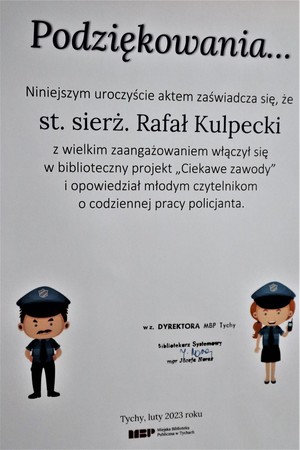 Na zdjęciu dyplom o treści: Podziękowanie Niniejszym uroczyście aktem zaświadcza się, że starszy sierżant Rafał Kulpecki z wielkim zaangażowaniem włączył się w biblioteczny projekt &quot;Ciekawe zawody&quot; i opowiedział młodym czytelnikom o codziennej pracy policjanta. Na dole Pieczątka dyrektora biblioteki oraz miejscowość i data: luty 2023. Po bokach dyplomy rysunek policjanta i policjantki.