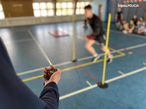 Na zdjęciu widoczna sala gimnastyczna. W tle widać biegnącego chłopca. Na pierwszym planie zdjęcia osoba trzymająca w ręku stoper.