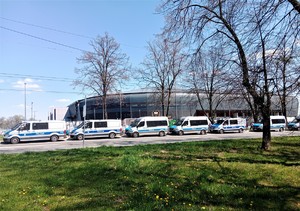 Na zdjęciu widoczna droga, wzdłuż której stoją policyjne radiowozy. W tle widoczny stadion.