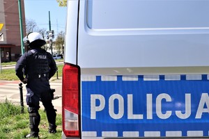 Na zdjęciu policyjny radiowóz i stający obok niego policjant z oddziałów prewencji.