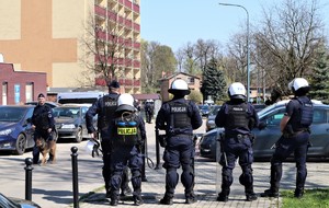 Na zdjęciu umundurowani policjanci oddziałów prewencji zabezpieczający przejście kibiców. Obok nich idący policjant z psem służbowym.