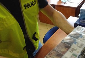 Policjant w kamizelce odblaskowej trzyma na biurku kartony z papierosami