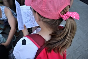 Na zdjęciu stojąca tyłem dziewczynka trzymająca w rękach biało-czarną książeczkę.
