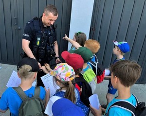 Na zdjęciu umundurowany policjant. Wokół niego grupa dzieci.