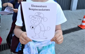 Na zdjęciu dziecko trzymające w rękach książeczkę z napisem Egzemplarz Bezpieczeństwa z narysowanym psem Sznupkiem.
