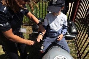 Na zdjęciu dziecko siedzące na motocyklu policyjnym. Obok niego policjanta zakładająca mu na rękę odblask.