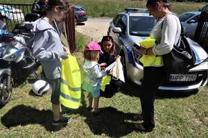 Na zdjęciu umundurowana policjanta, która wręcza uczestnikom pikniku kamizelki odblaskowe i elementarz bezpieczeństwa.