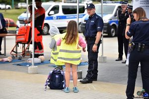 Na zdjęciu namiot z napisem Komenda Miejska Policji w Tychach. Obok namiotu umundurowani policjanci i dziewczynka stojąca tyłem, zakładająca kamizelkę odblaskową.