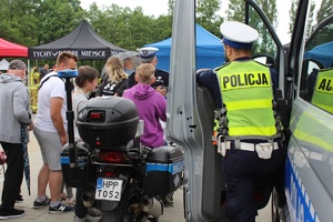 Na zdjęciu motocykl policyjny i radiowóz. Przy pojazdach dwóch umundurowanych policjantów Ruchu Drogowego oraz osoby uczestniczące w pikniku.