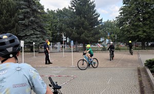 Na umundurowany policjant oraz dzieci jeżdżące na rowerach. Dzieci mają założone kaski rowerowe.