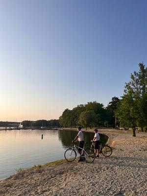 Na zdjęciu dwóch umundurowanych policjantów stojących przy rowerach na brzegu jeziora.