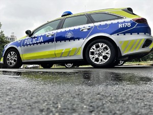 Na zdjęciu oznakowany radiowóz policyjny na mokrym asfalcie.