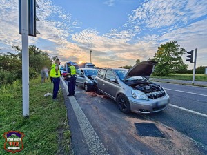 Na zdjęciu policjanci w kamizelkach odblaskowych stojący na poboczu drogi. Obok nich na jezdni dwa uszkodzone samochody.