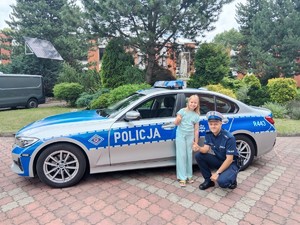 Na zdjęciu radiowóz policyjny. Obok niego policjant i dziewczyna którzy pozują do zdjęcia.