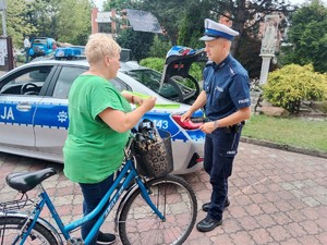 Na zdjęciu policjant raz kobieta na rowerze na tle policyjnego radiowozu.