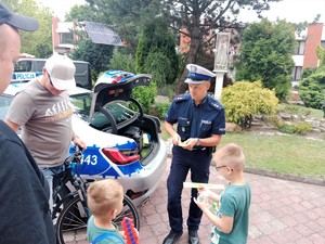 Na zdjęciu policjant rozdający odblaski dzieciom. W tle radiowóz.