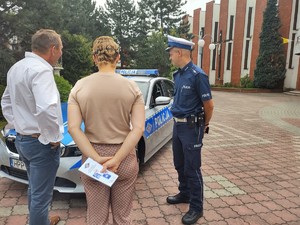 Na zdjęciu policjant rozmawiający z kobietą i mężczyzną przy radiowozie.