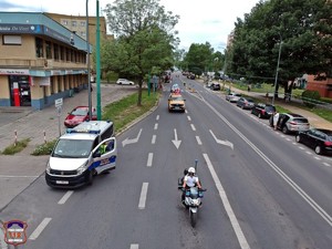 Zdjęcoie z góry przedstawiające policjanta ruchu drogowego na motocyklu. Za nim pojazd przewożący biskupa, który święci pojazdy oraz radiowóz.