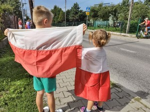 Na zdjęciu dwoje dzieci stojących tyłem i owiniętych flagami Polski.