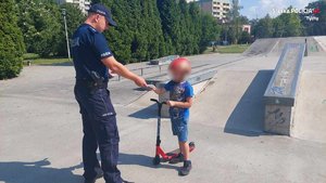 Umundurowany policjant daje ulotkę chłopcu na hulajnodze.