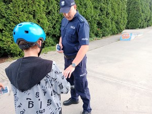 Umundurowany policjant daje ulotkę chłopcu na hulajnodze.