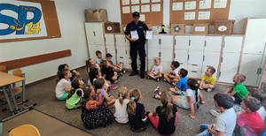 Na zdjęciu umundurowany policjant stojący przed grupą dzieci w sali lekcyjnej.