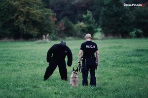 Pozorant ubrany w specjalny kombinezon, policjant i pies przygotowany do ćwiczeń.