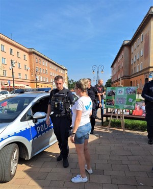Na zdjęciu umundurowany policjant oraz kobieta, którzy stoją obok radiowozu.
