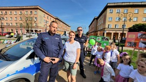 Na zdjęciu dwóch umundurowanych policjantów, kobieta oraz dzieci. Wszyscy stoją obok radiowozu.