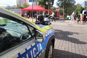 Na zdjęciu policyjny radiowóz.  Przed nim policyjny motocykl. W tle wóz straży pożarnej.