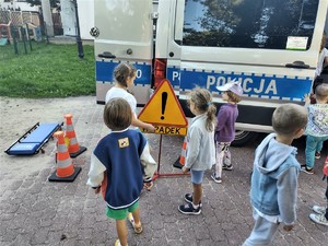Na zdjęciu grupa przedszkolaków oraz policjant ruchu drogowego obok radiowozu.