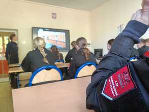 Na zdjęciu uczniowie klasy mundurowej w sali lekcyjnej. Przed nimi umundurowana policjantka.