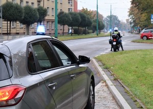 Na zdjęciu nieoznakowany radiowóz z sygnałem świetlnym na dachu.  Przed nim policjant na służbowym motocyklu.