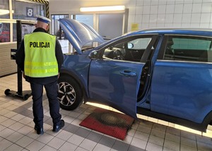 Na zdjęciu umundurowany policjant ruchu drogowego stojący obok samochodu na stacji diagnostycznej.