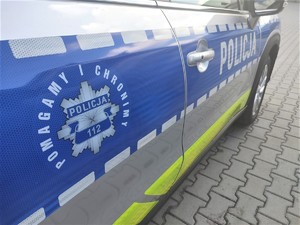Na zdjęciu bok radiowozu policyjnego z logo Policji oraz napisem Pomagamy i chronimy.