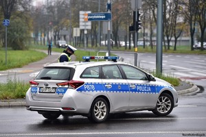 Na zdjęciu radiowóz policyjny oraz stojący przy nim umundurowany policjant.