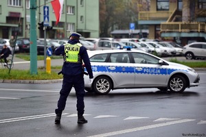 Na zdjęciu radiowóz policyjny oraz policjant kierujący ruchem na skrzyżowaniu.