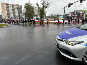 Na zdjęciu radiowóz policyjny. W tle widać uczestników biorących udział w obchodach Dnia Niepodległości.