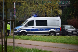 Na zdjęciu radiowóz oraz umundurowany policjant w kamizelce odblaskowej.