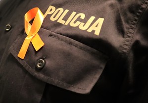 Na zdjęciu napis Policja na koszuli służbowej z przypiętą wstążką koloru pomarańczowego.