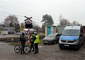 Na zdjęciu umundurowani policjanci i rowerzysta. W tle tory kolejowe oraz radiowóz.