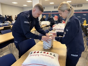 Na zdjęciu umundurowana policjantka i policjant podczas pakowania prezentów.