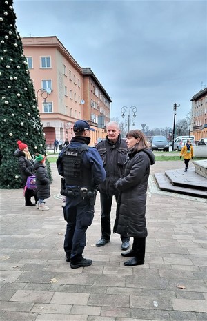 Na zdjęciu umundurowany policjant rozmawiający z mężczyzną i kobietą.
