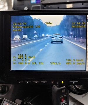 Zdjęcie przedstawia kadr z nagrania policyjnego wideorejestratora, na którym widać pomiar prędkości samochodu jadącego przed radiowozem. Pomiar wskazuje 164 kilometry na godzinę.