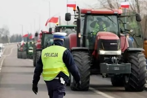 Na zdjęciu umundurowany policjant na drodze. W tle ciągniki rolnicze.