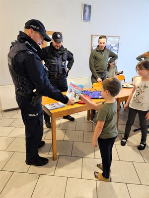 Na zdjęciu umundurowani policjanci podczas spotkania z dziećmi uczestniczącymi w półkolonii.