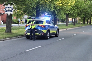 Na zdjęciu policjanci ruchu drogowego stojący obok radiowozu z włączonymi sygnałami świetlnymi.