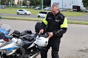 Na zdjęciu policjant zakładający kask obok motocykla.