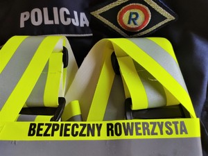 Na zdjęciu odblaskowe szelki z napisem Bezpieczny rowerzysta oraz napis policja i logo ruchu drogowego.